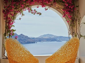 A room with a large arched window overlooking a body of water and hills. - Andronis Luxury Suites (Santorini)