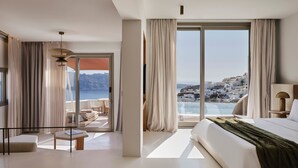 Una habitación de hotel moderna con una cama grande, un balcón con vistas al mar y un comedor.