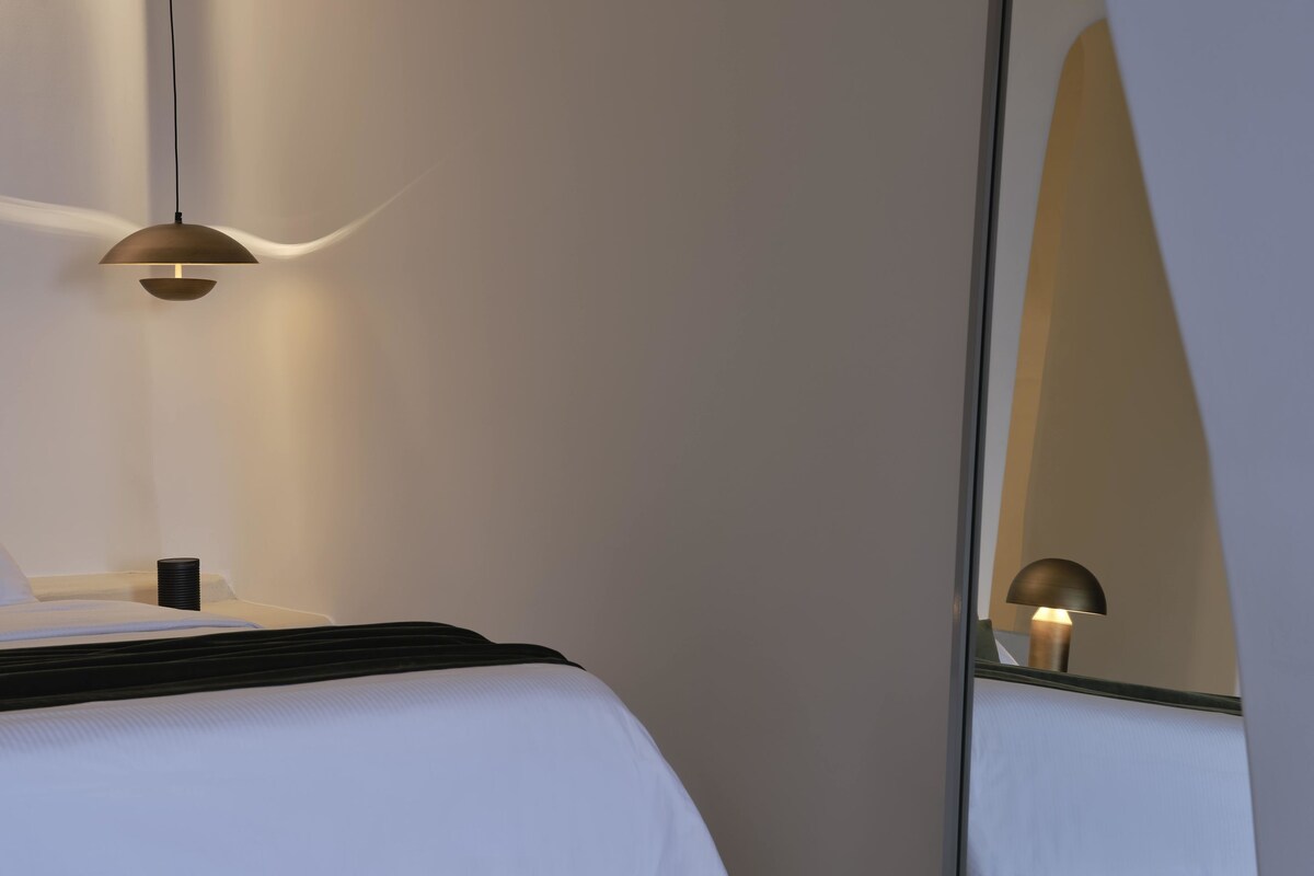 Una habitación de hotel moderna con cama, mesita de noche, lámpara y un espejo grande.
