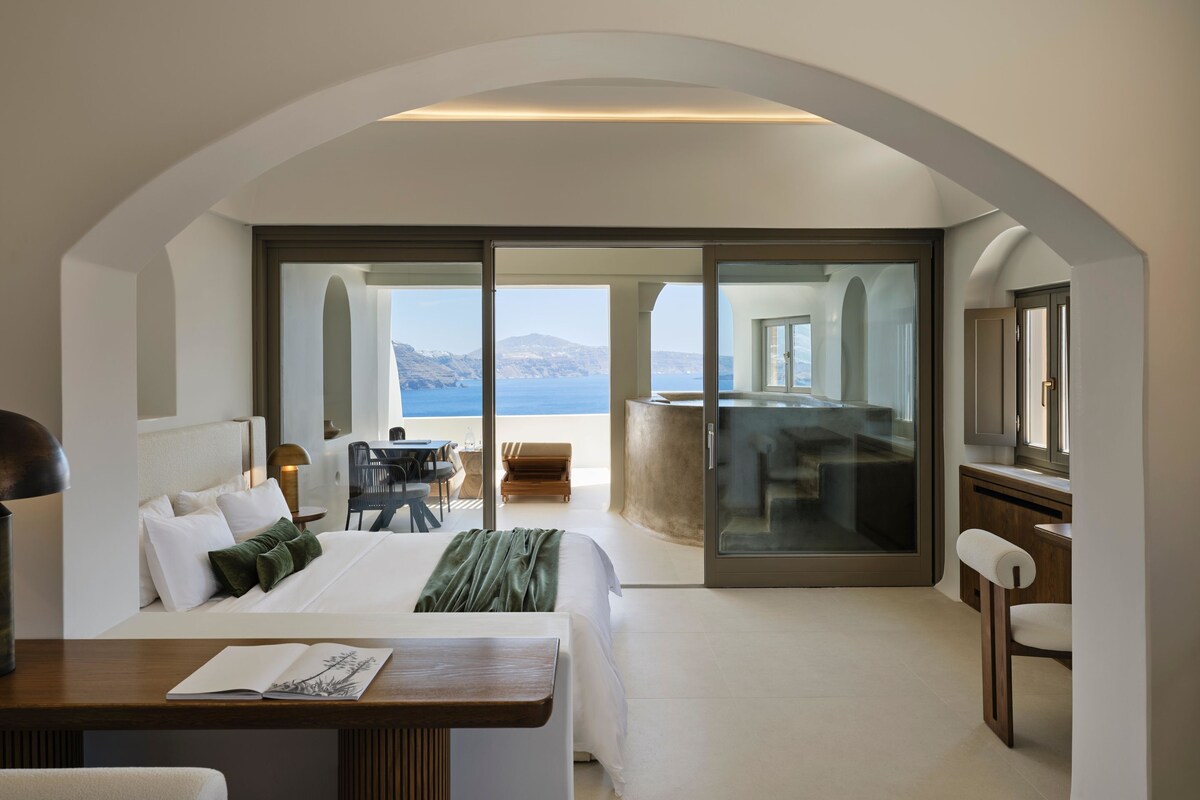 Una habitación de hotel moderna con una cama grande, un escritorio y un balcón con vistas al mar.
