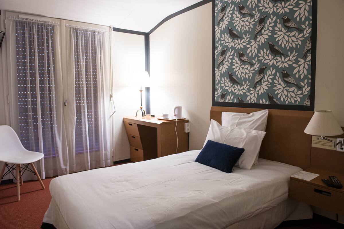 Una habitación de hotel con una cama, un escritorio, una silla y una pared con un motivo de pájaros.