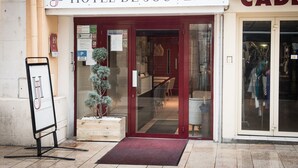 Exterior del Hotel de Juvence, con una puerta roja, una planta pequeña en maceta y un letrero.
