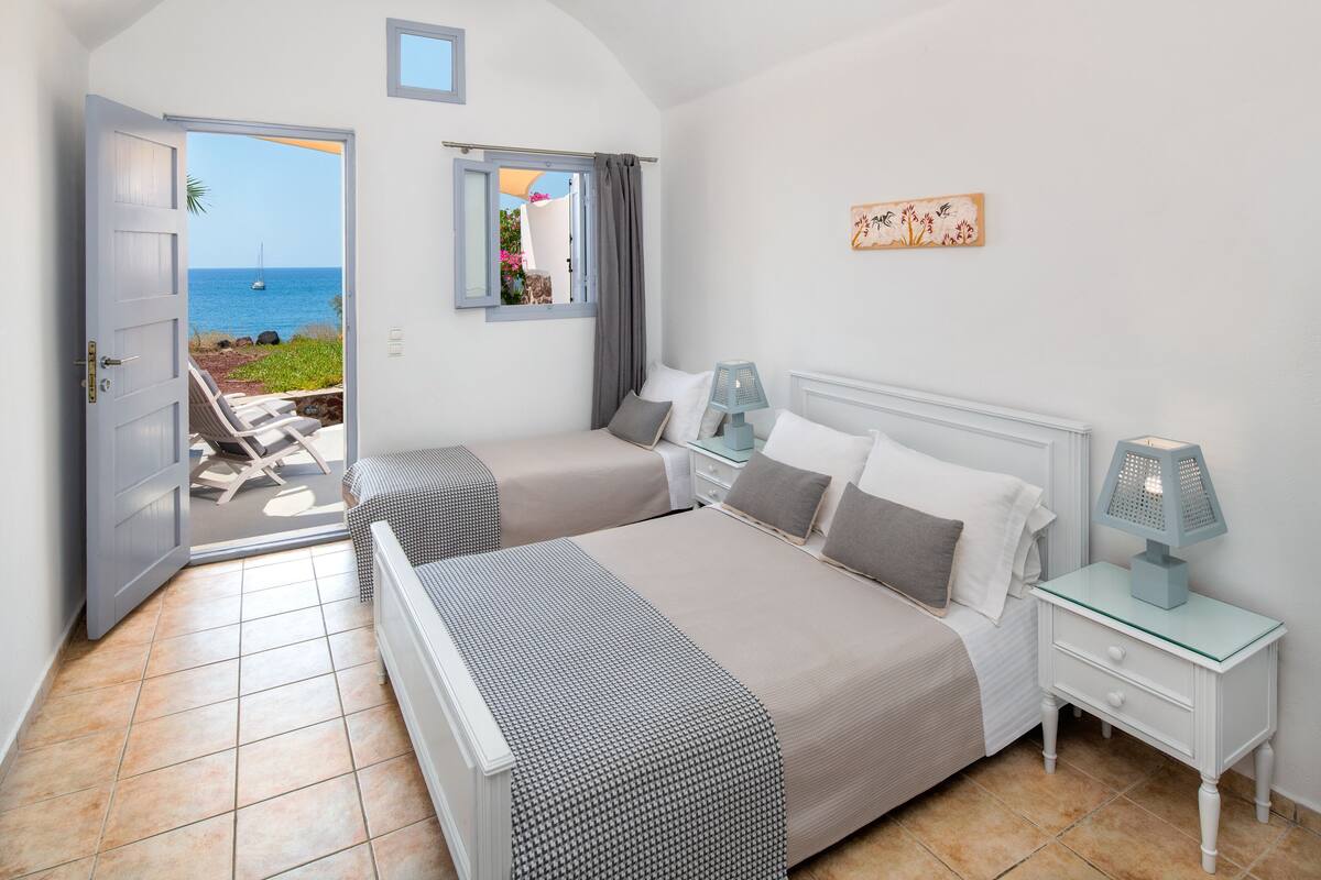 A bedroom with two beds, a view of the sea, and a balcony with chairs.