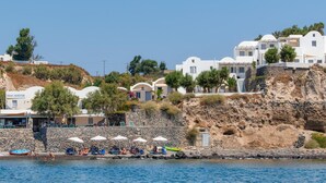 Un hotel a la costa amb edificis blancs, una paret de pedra i para-sols de platja.