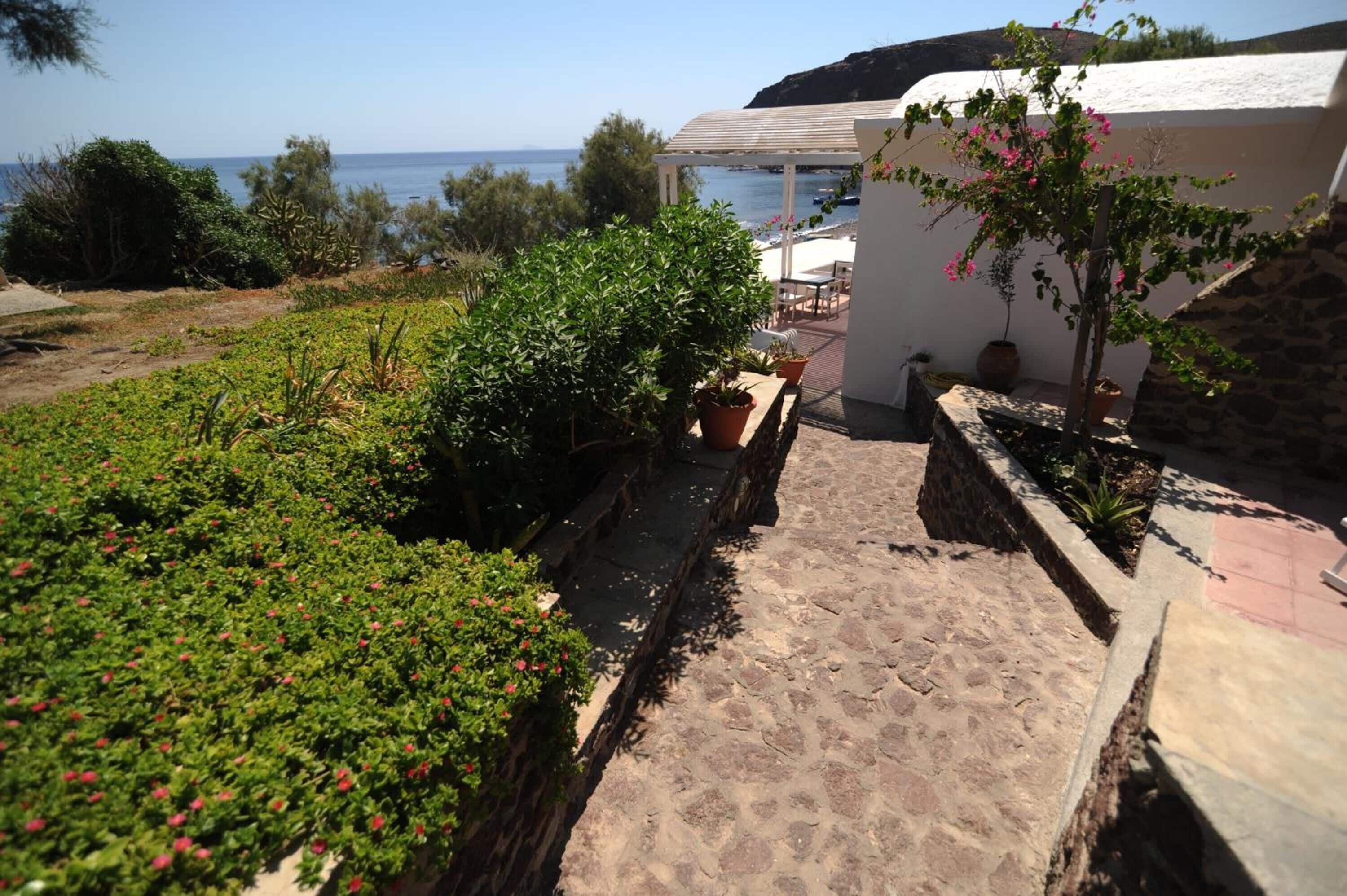 A garden with potted plants and a stone pathway leading to a white building with a pergola.