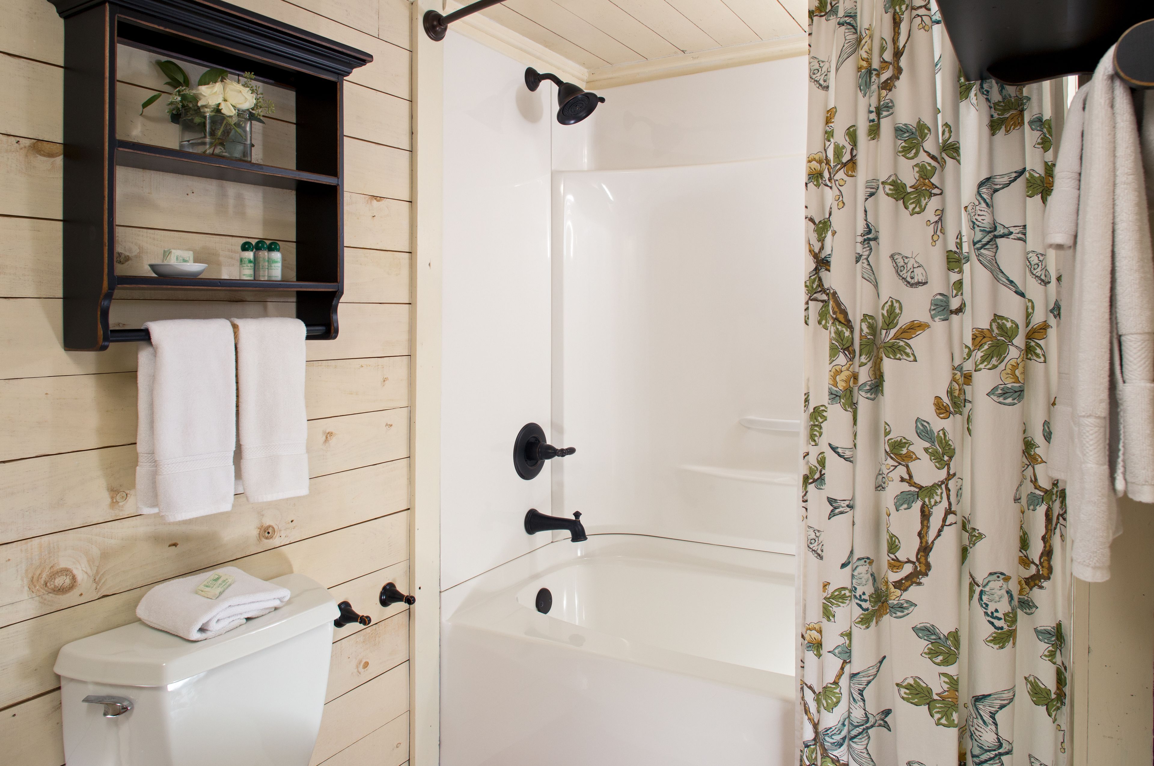 A bathroom with a white bathtub, a wooden vanity with a shelf, and a shower curtain with a bird pattern.
