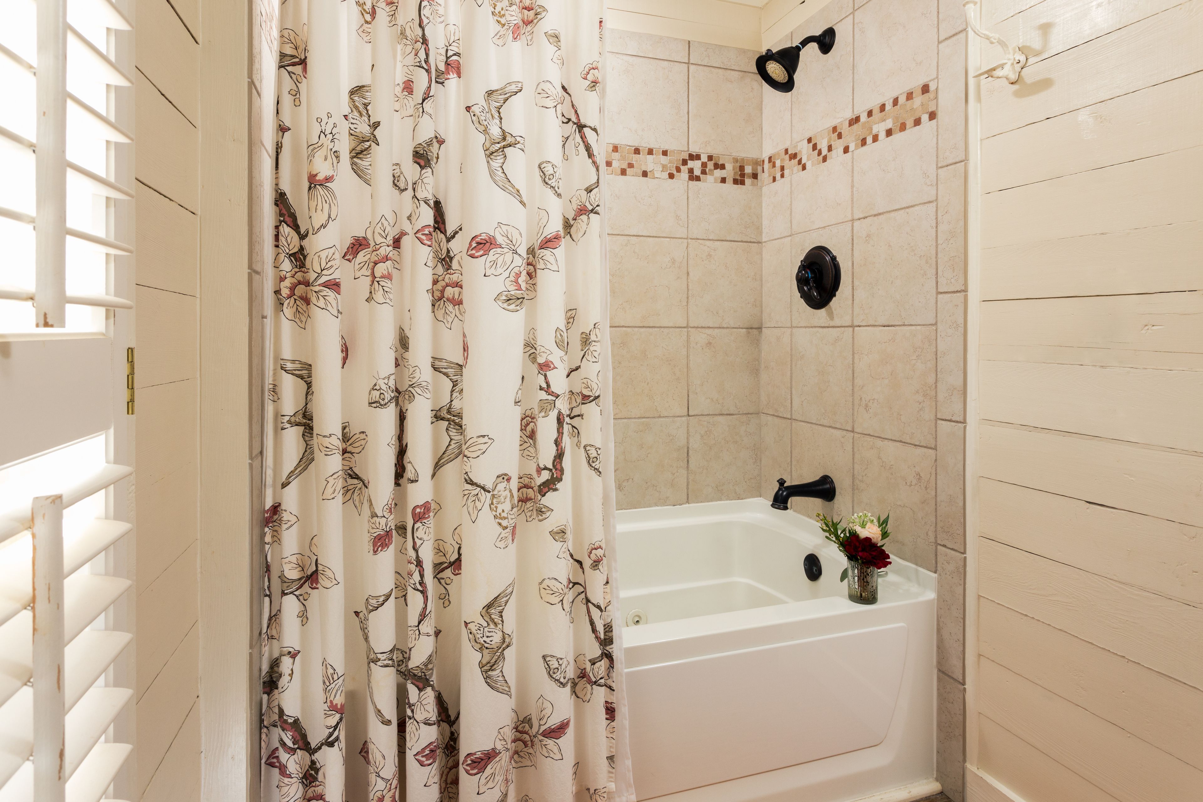 Un baño con ducha, bañera y ventana con persianas.