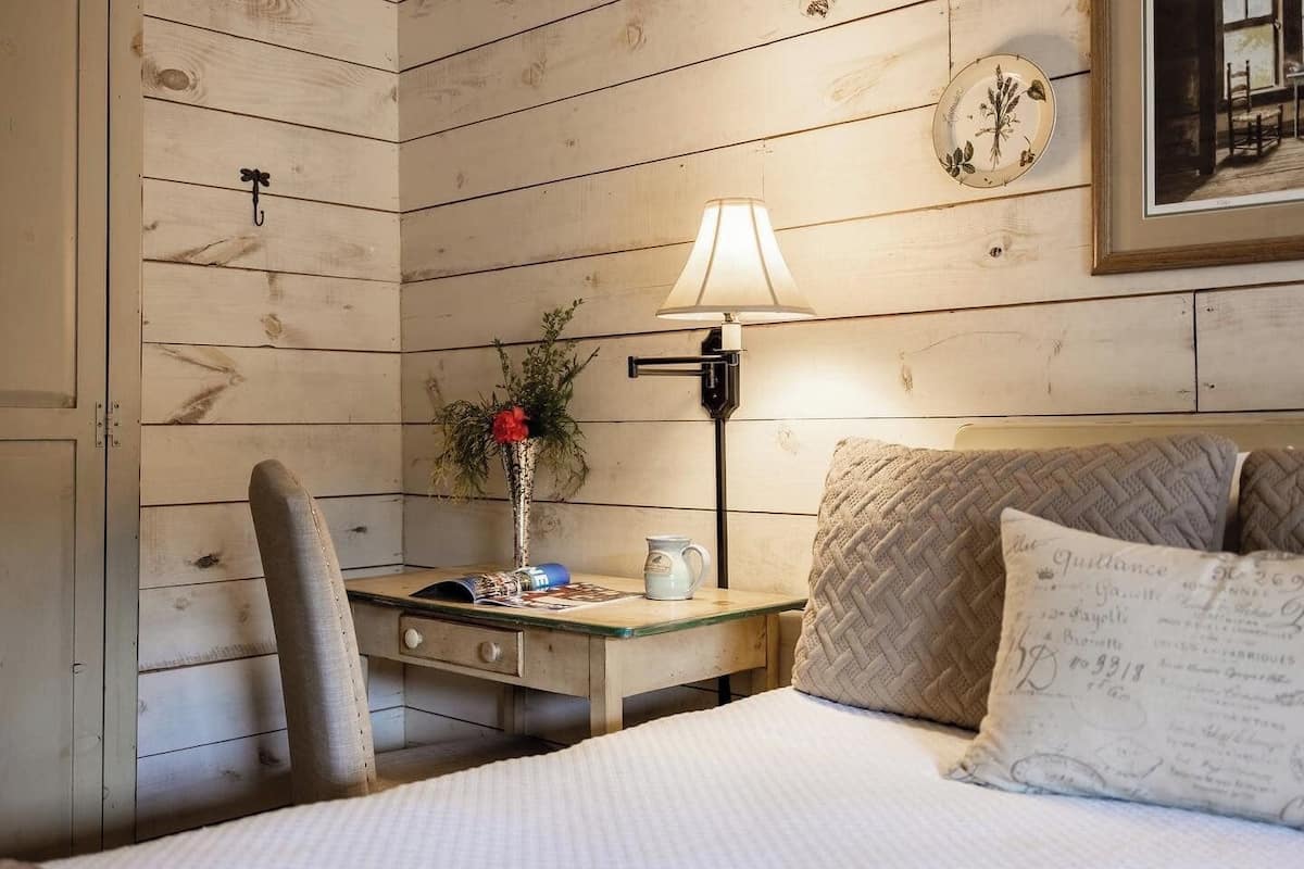A wooden-paneled room with a bed, a desk, a lamp, and a framed picture on the wall.
