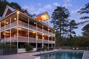 Eine zweistöckige Holzhütte mit Balkon, Schwimmbad und einer Terrassenfläche.