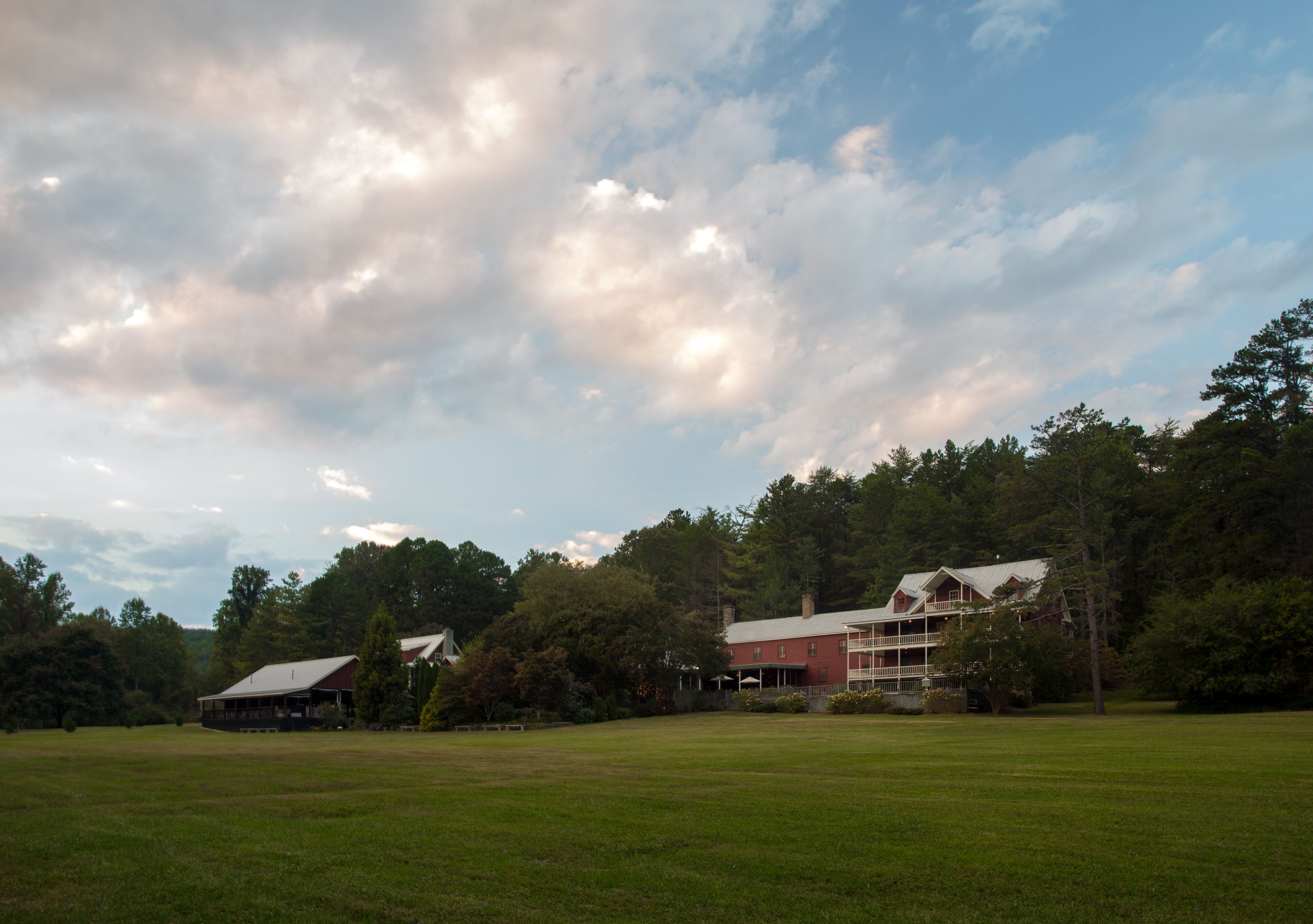 A large, open grassy field with a red barn and a two-story house with a porch.