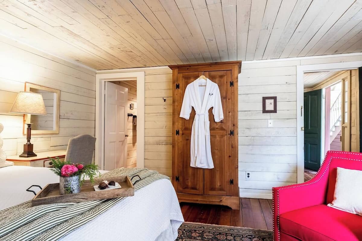 A room with a bed, a red chair, a wooden wardrobe, and a wooden door.