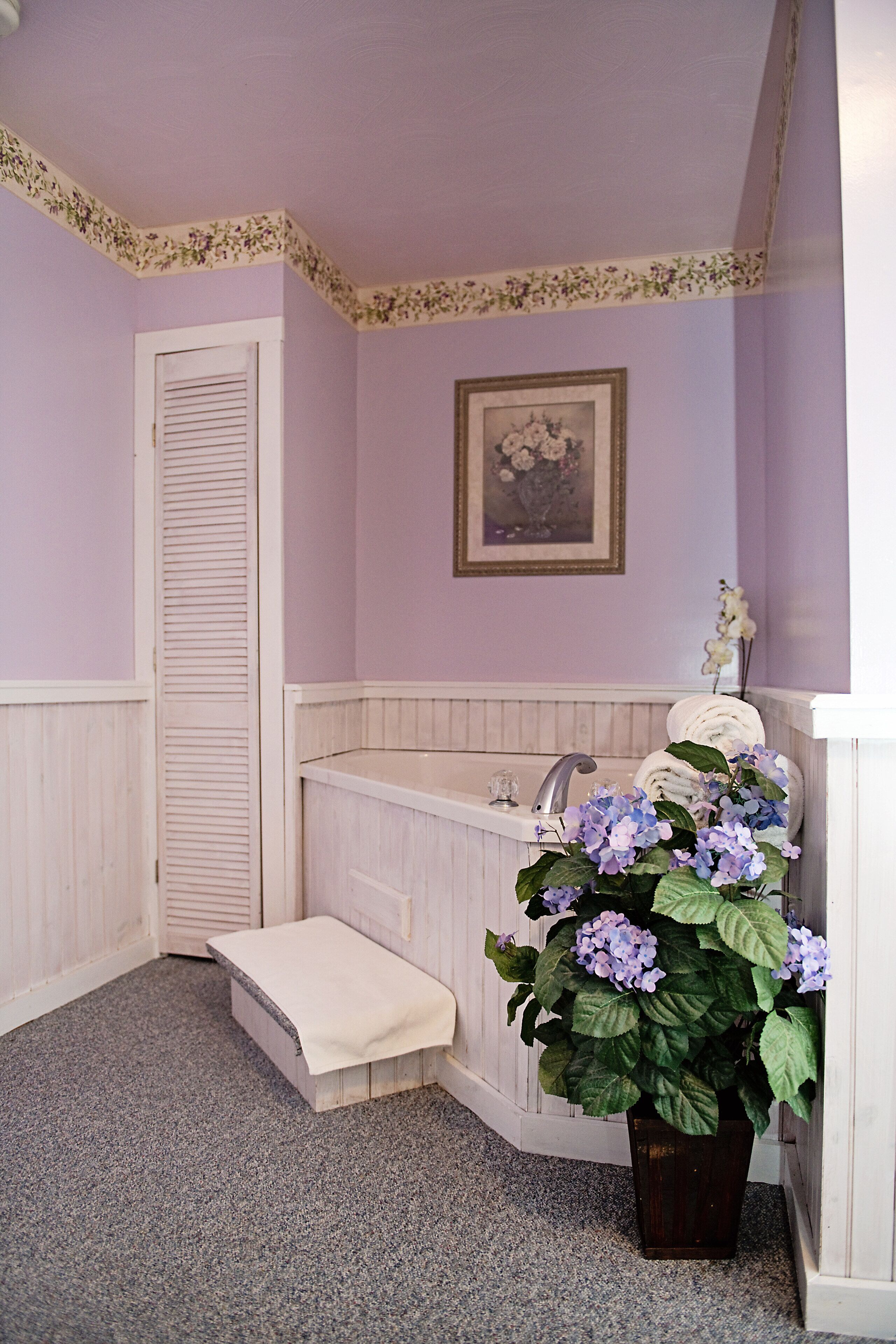 A bathroom with a bathtub, a sink, a step leading to a door, and a potted plant with flowers.