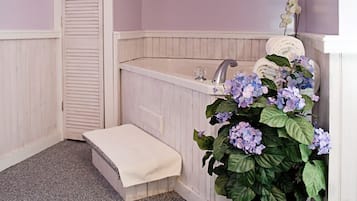 A bathroom with a bathtub, a sink, a step leading to a door, and a potted plant with flowers.