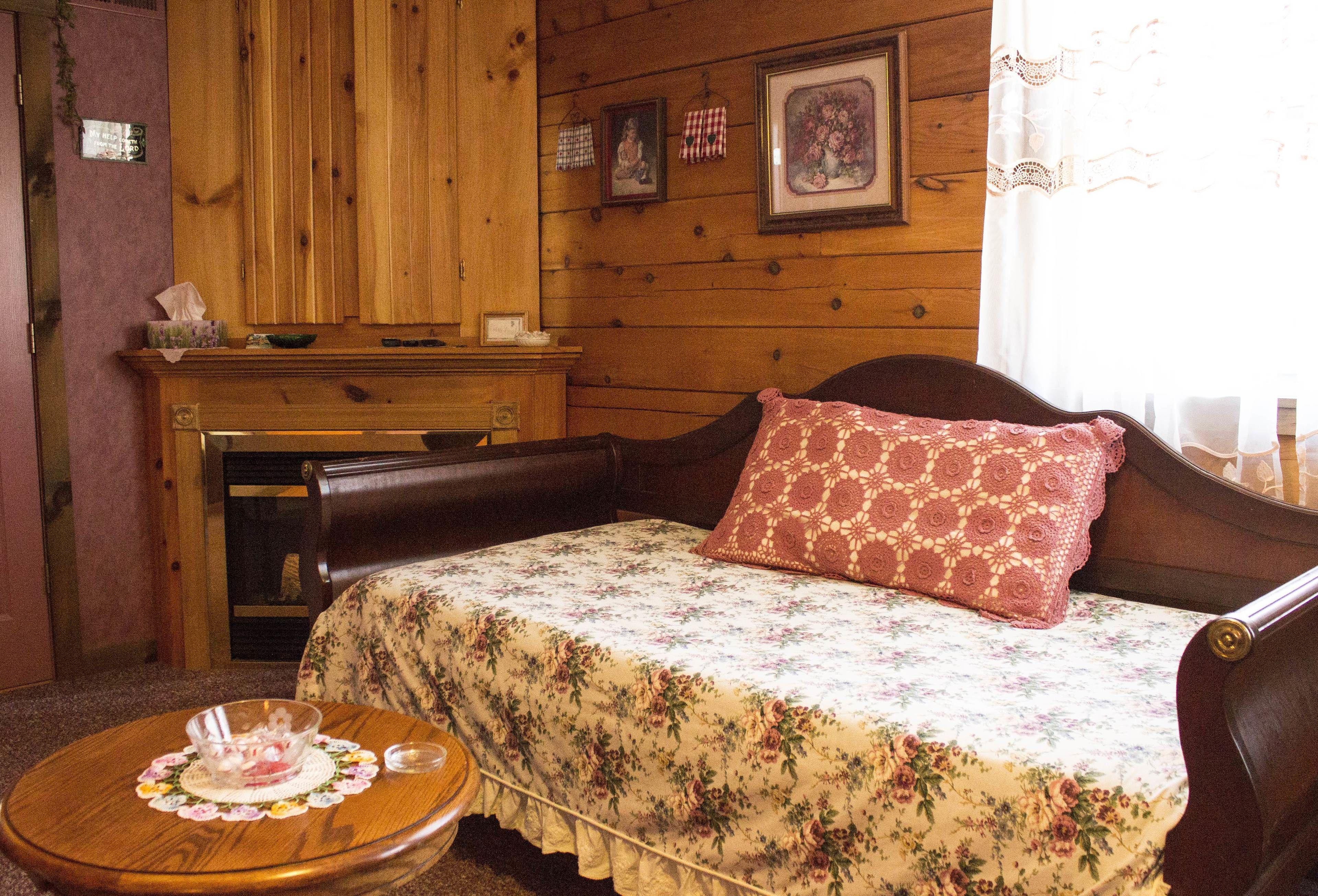 A cozy room with a wooden cabin-style interior, a bed with floral bedding, a wooden dresser, and a small round table with a glass container.