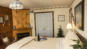 A bedroom with a bed, a bedside table, a lamp, a small Christmas tree, and a fireplace.