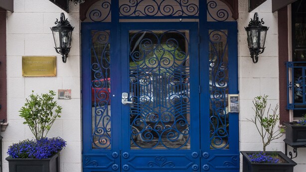 A building facade with a blue ornate entrance, a sign reading "Monte Cristo," and two potted plants on the ground.