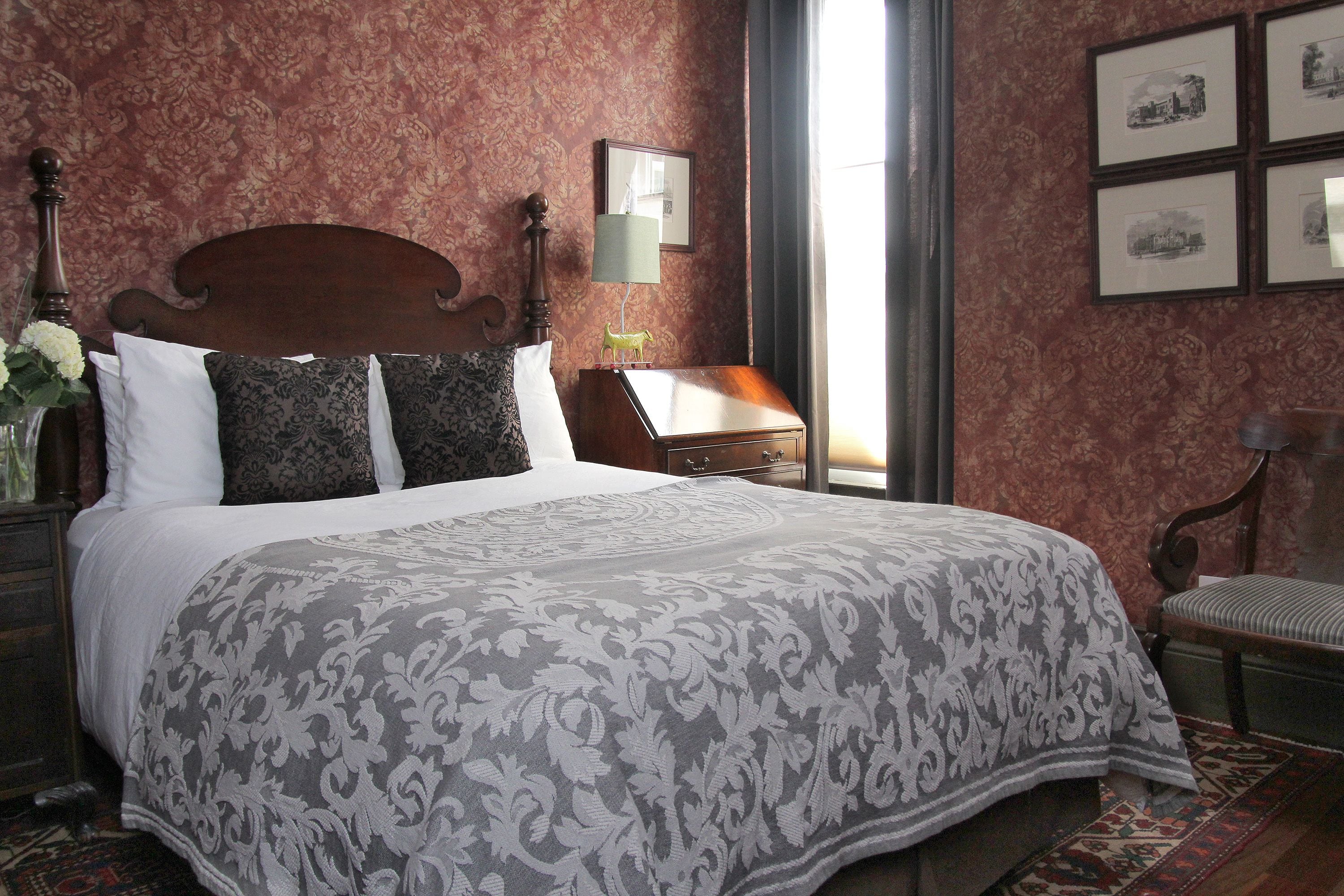 A neatly made bed with a patterned bedspread, a wooden headboard, and a nightstand with a lamp and a small decorative item.