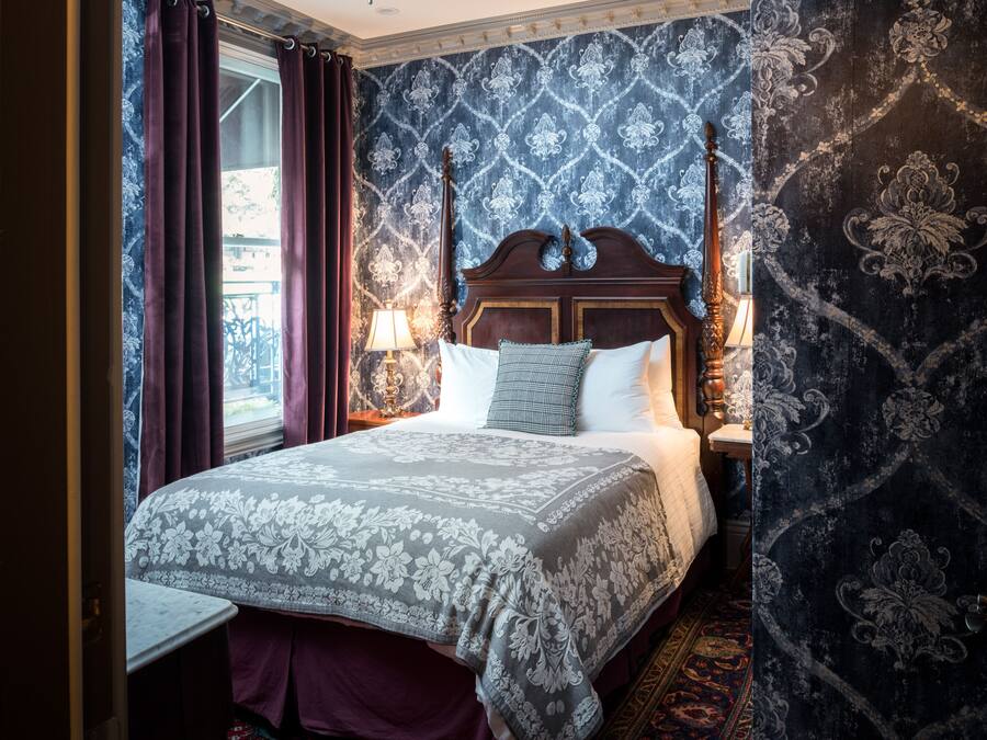 Une chambre à coucher avec un lit à baldaquin, une table de chevet avec une lampe et un papier peint à motifs.