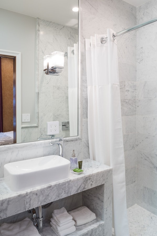 A bathroom with a white sink, marble countertop, and a glass shower enclosure.