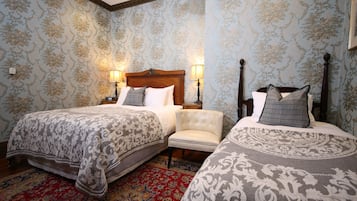 A hotel room with two beds, a red patterned rug, and floral wallpaper.