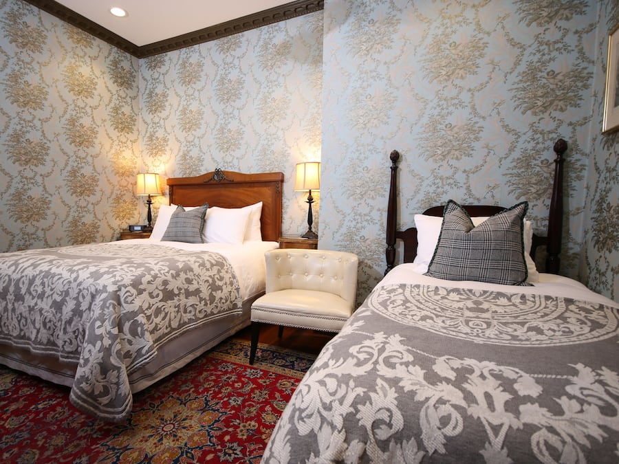 A hotel room with two beds, a red patterned rug, and floral wallpaper.
