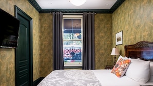 A hotel room with a large bed, a television, a window with curtains, and a framed picture on the wall.