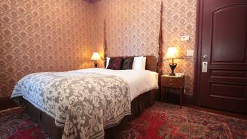 A hotel room with a large bed, two bedside tables with lamps, a wooden door, and patterned wallpaper.