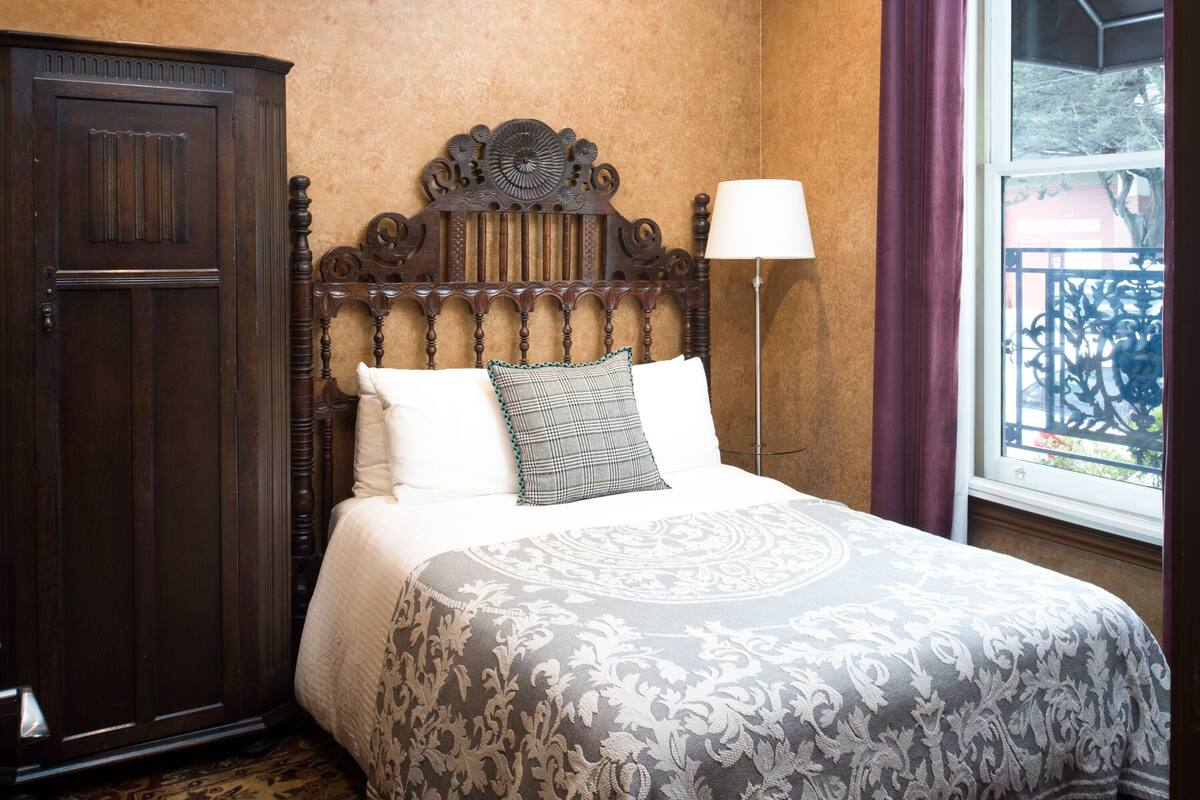 A bedroom with a large bed, a wooden headboard, a floor lamp, and a window with a view of a balcony.