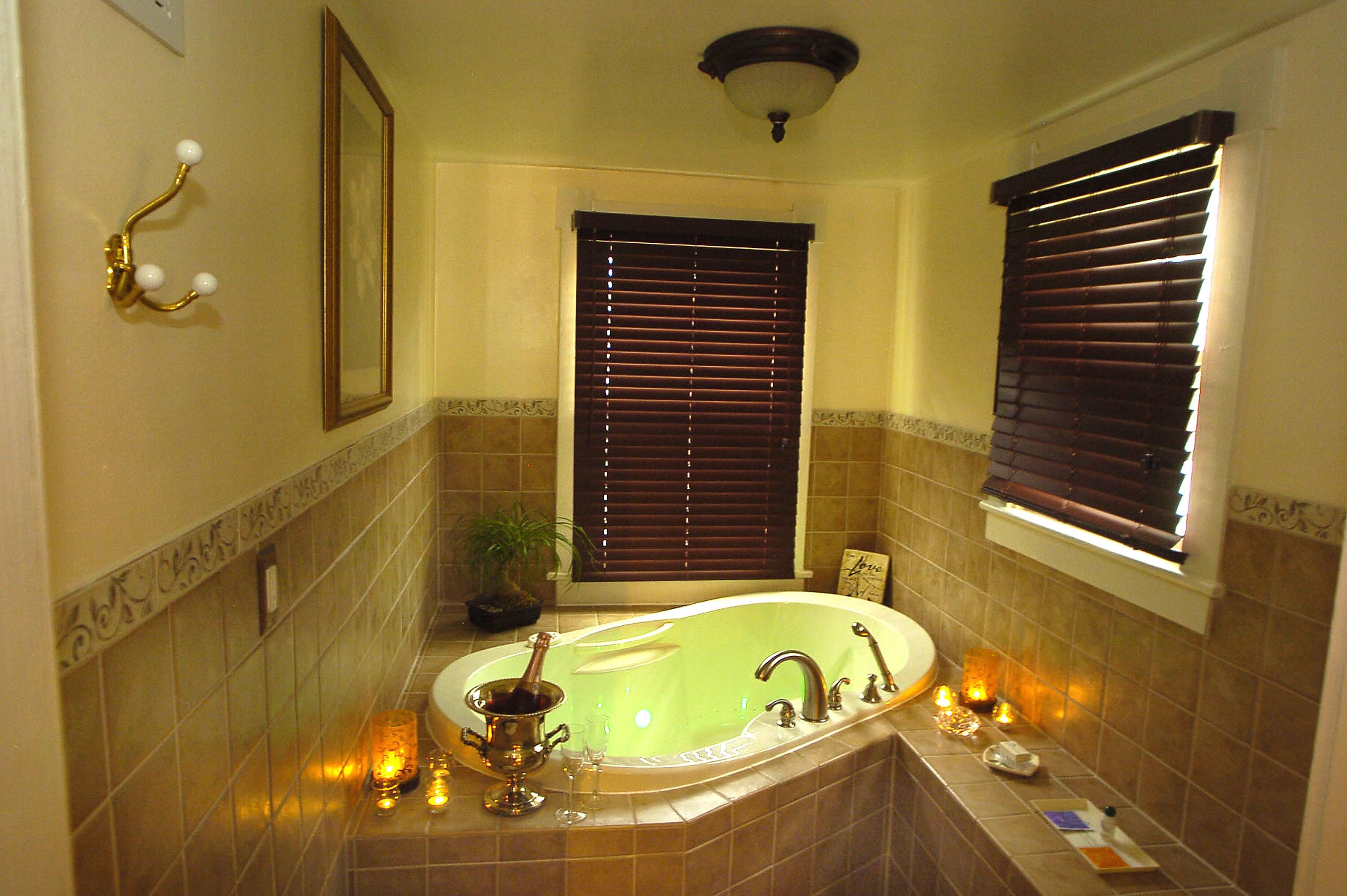 A bathroom with a freestanding bathtub, a mirror, a wall-mounted light fixture, and a window with blinds.