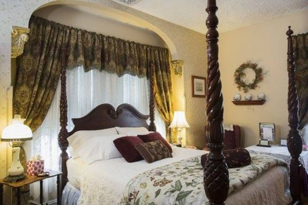 A four-poster bed with a canopy, a bedside table with a lamp, and a wall-mounted shelf with decorative items.