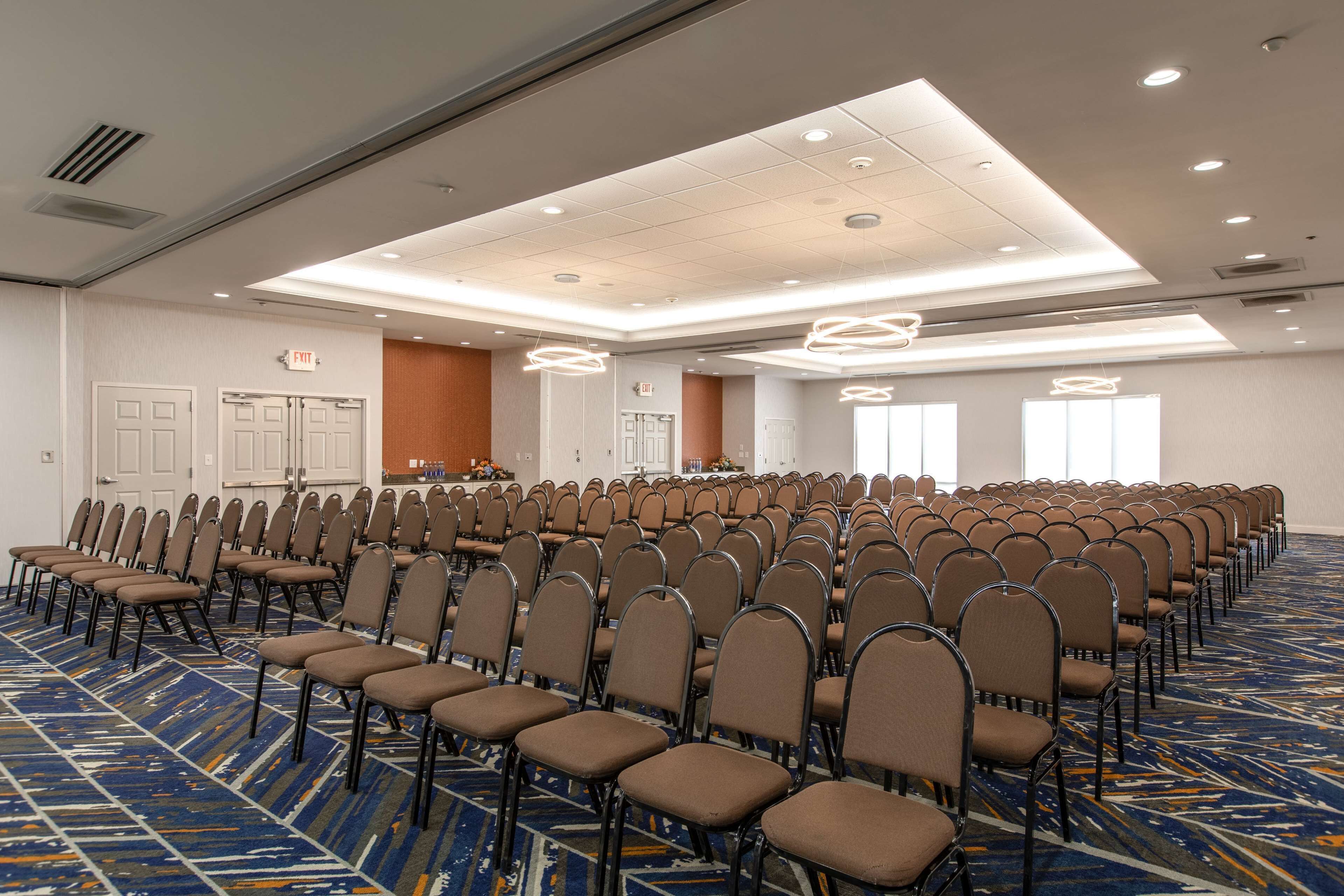 Une salle de conférence avec des rangées de chaises, une moquette à motifs et des luminaires au plafond.