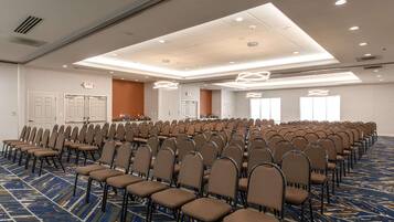 Une salle de conférence avec des rangées de chaises, une moquette à motifs et des luminaires au plafond.