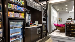 A coffee shop interior with a refrigerated display case, a coffee machine, and a variety of packaged snacks.