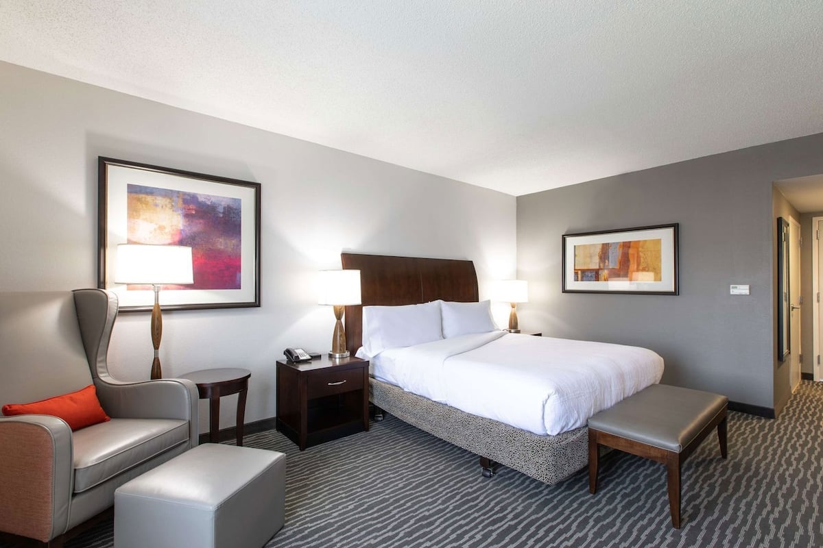 A hotel room with a bed, two bedside tables, a chair, a bench, and two wall-mounted lamps.