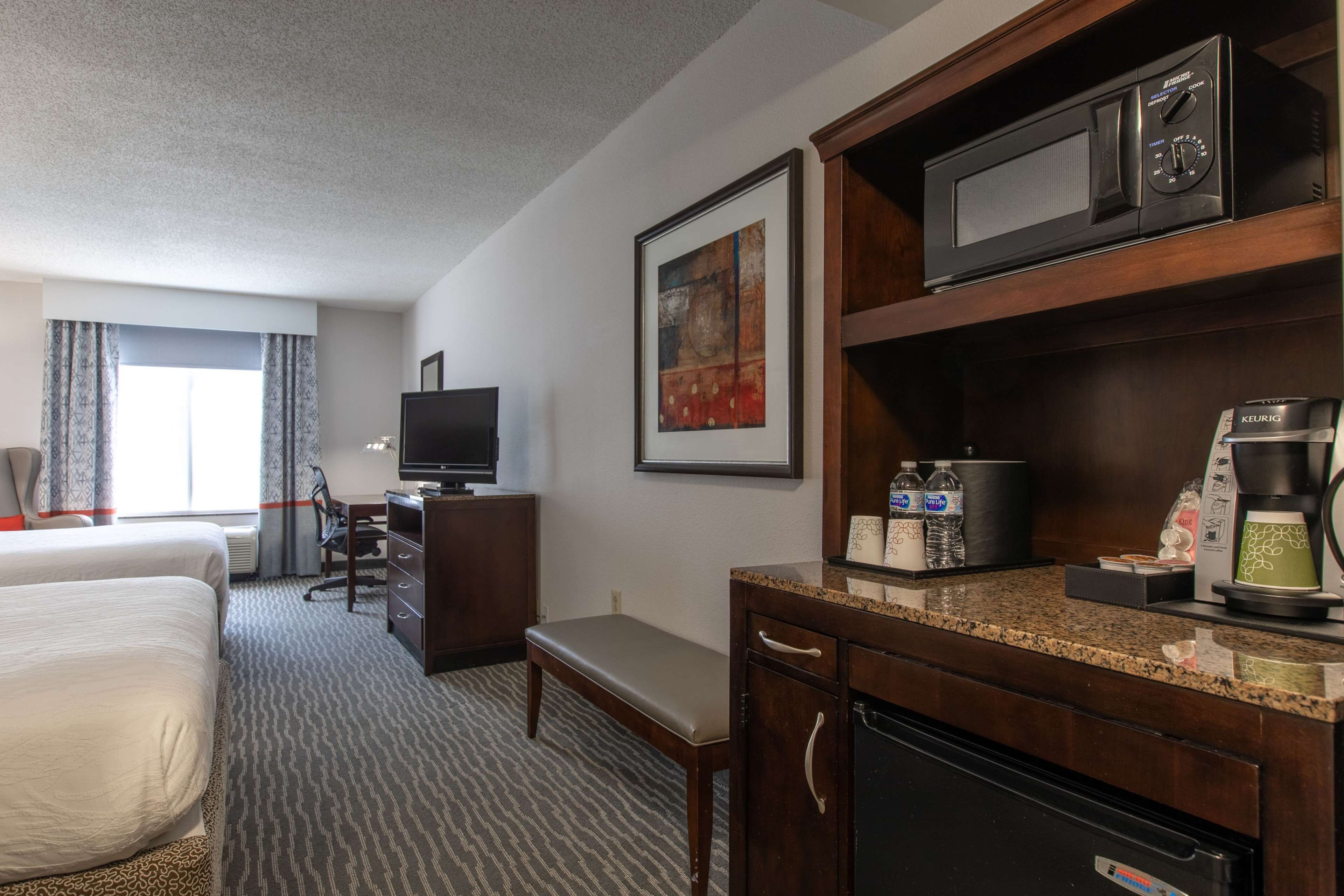 Een hotelkamer met een bed, bureau, televisie, magnetron, koffiezetapparaat en een schilderij aan de muur.