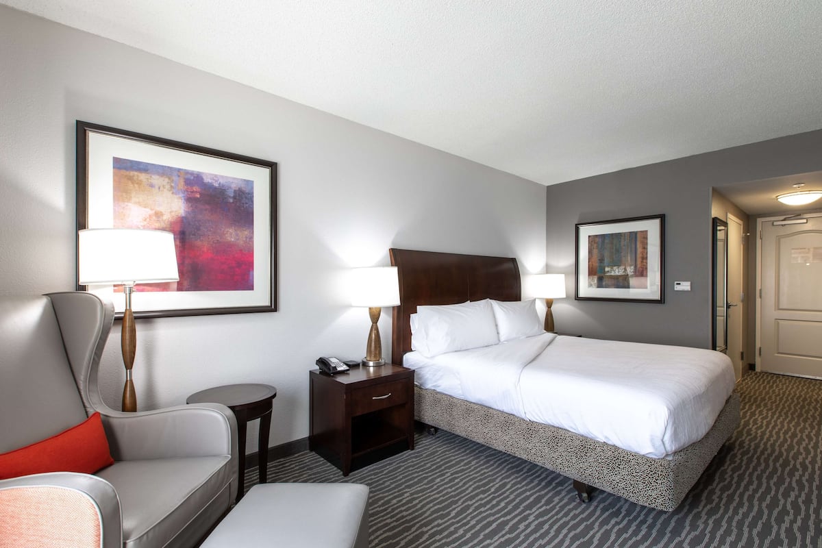 A hotel room with a bed, a chair, a nightstand, and two lamps.