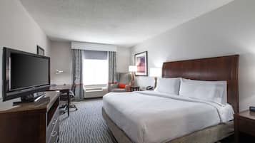 A hotel room with a large bed, a flat-screen TV, a desk with a computer, a chair, and a window with curtains.