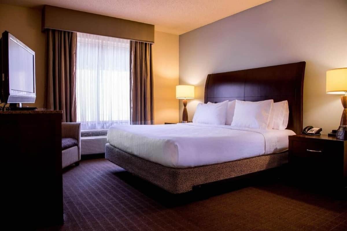 A hotel room with a large bed, a television, a desk, and a window with curtains.