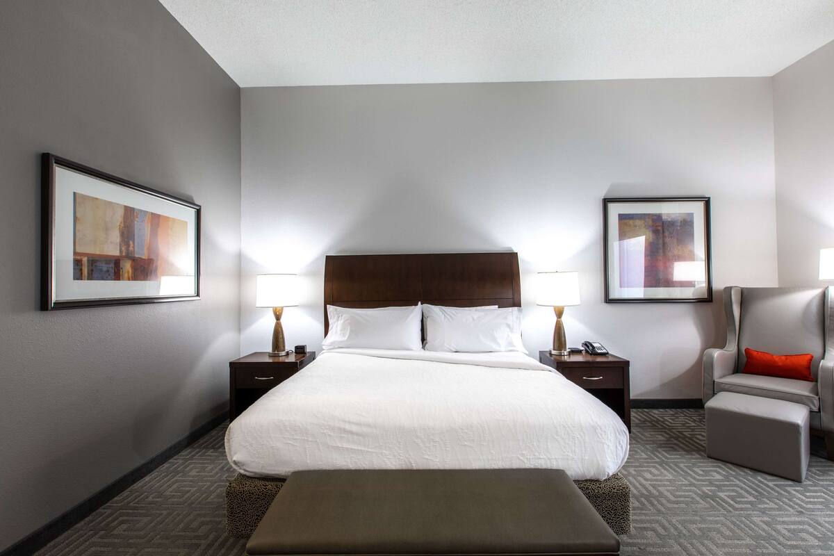 A hotel room with a large bed, two bedside tables, a chair, and two framed pictures on the walls.