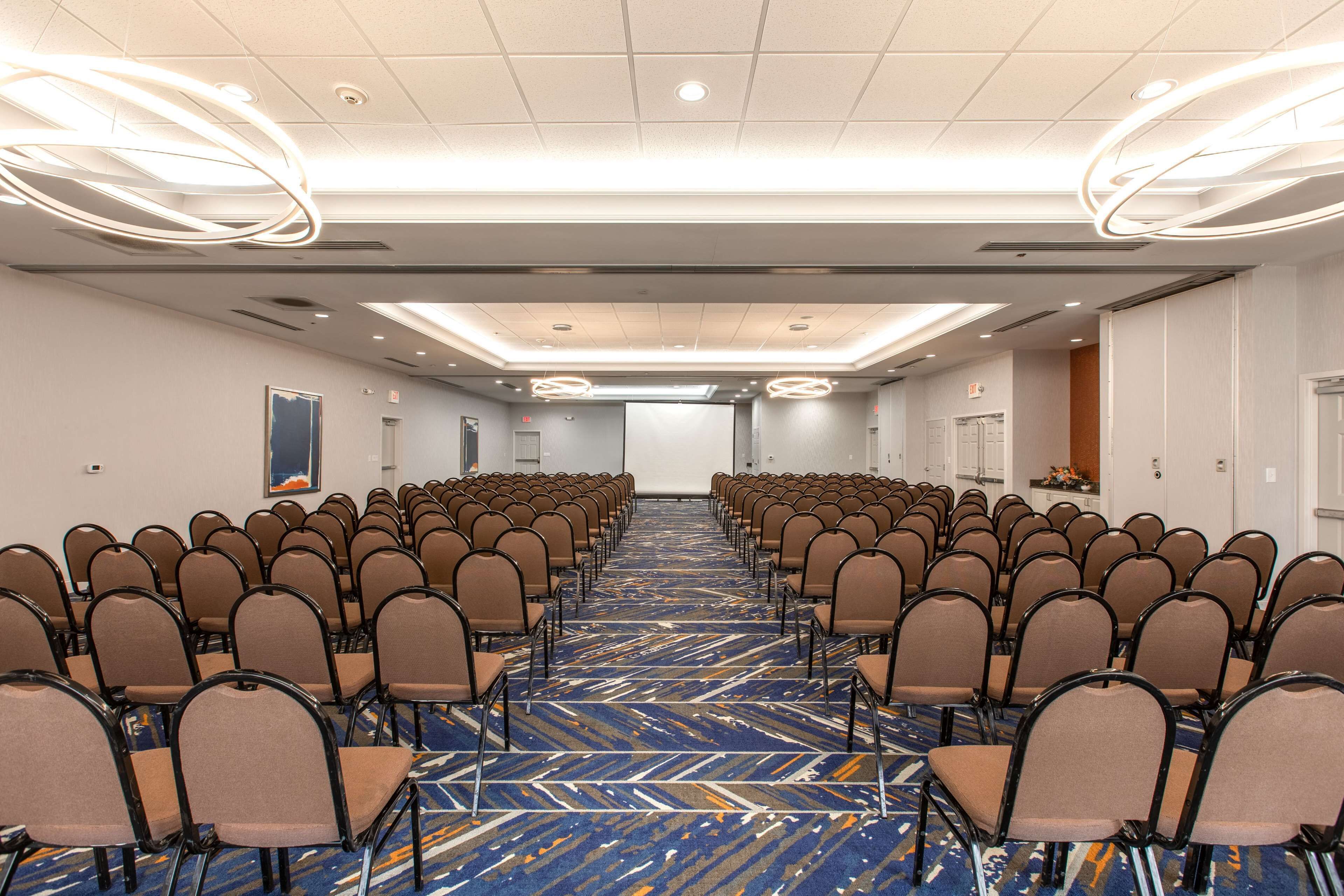 A conference room with rows of chairs, a patterned carpet, and modern lighting fixtures.