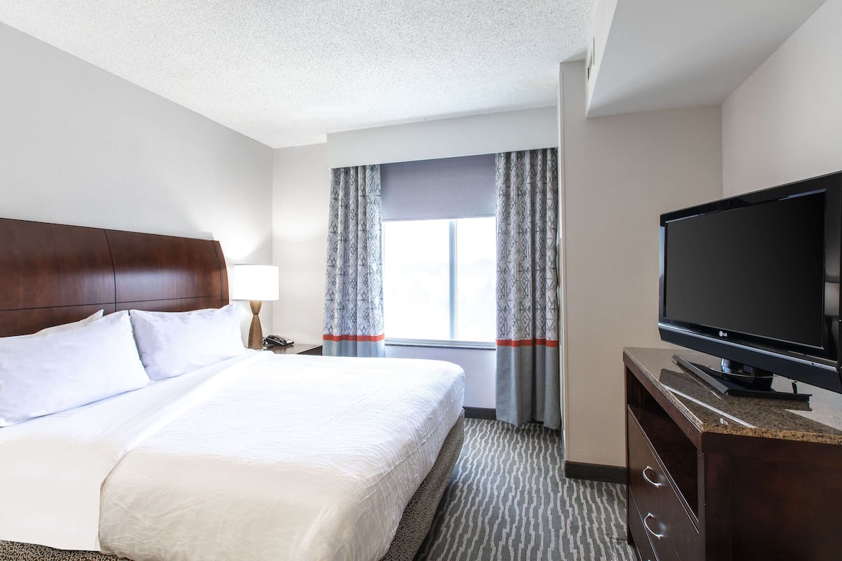 A hotel room with a large bed, a flat-screen TV, a dresser, and a window with curtains.