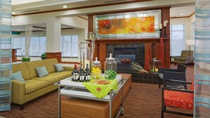 A modern hotel lobby with a sofa, a coffee table with drinks, a fireplace, and a large abstract painting. - Hilton Garden Inn Austin North (Austin)