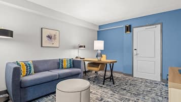 A modern room with a blue accent wall, a sofa with patterned cushions, a desk with a lamp, and a door.
