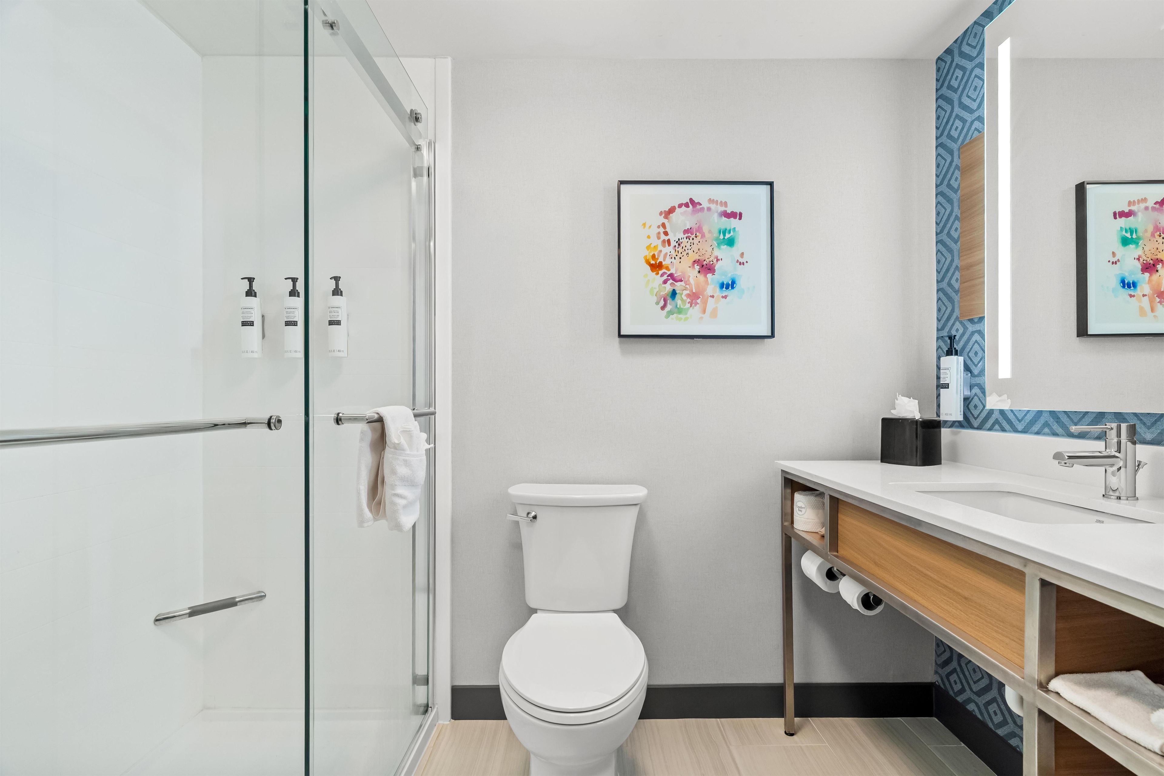 Un baño moderno con cabina de ducha de vidrio, inodoro blanco, lavabo con espejo y dos cuadros en la pared.