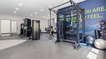 Un gimnasio con equipo de ejercicio diverso, incluyendo una jaula para sentadillas, cintas de correr y pesas sueltas.