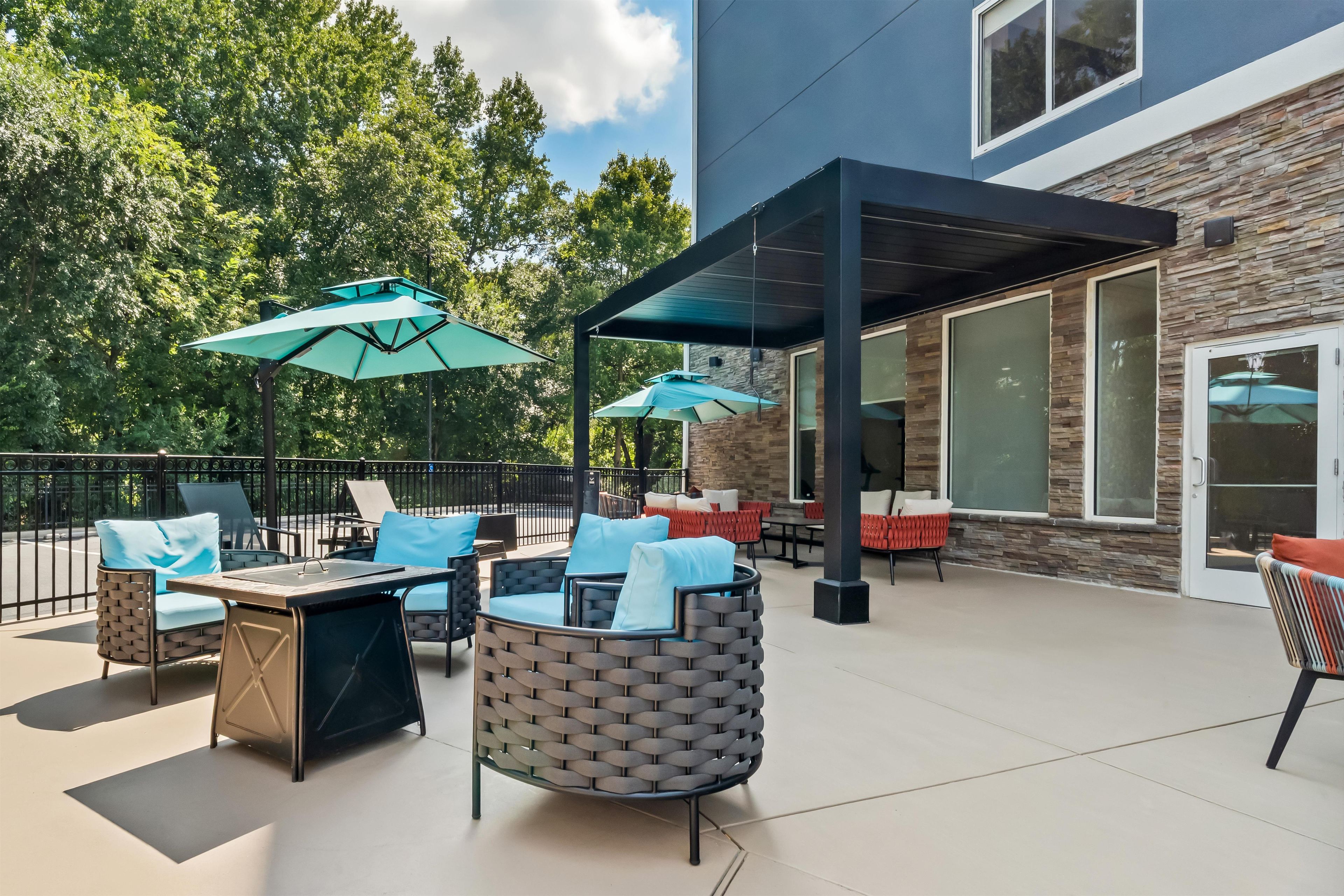 An outdoor patio with seating, umbrellas, and a building with stone facade and large windows.