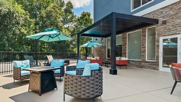 An outdoor patio with seating, umbrellas, and a building with stone facade and large windows.