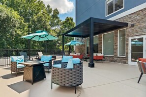 An outdoor patio with seating, umbrellas, and a building with stone facade and large windows. - Hilton Garden Inn Gainesville (Gainesville)