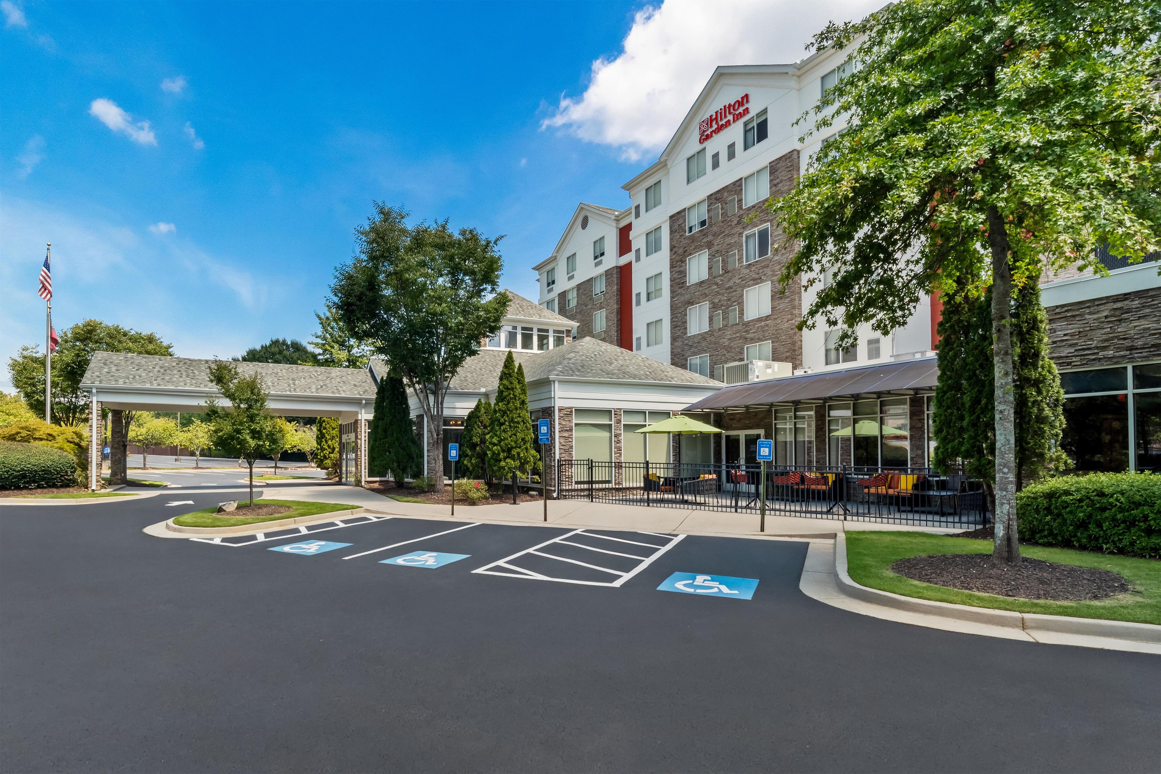A hotel entrance with handicap parking, a covered waiting area, and a building with a garden view.