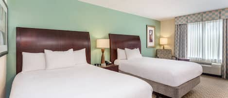 Habitación de hotel con dos camas, una mesita de noche con lámpara, un cuadro en la pared y una ventana con cortinas.